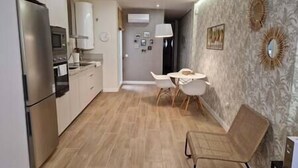 A compact kitchen with modern appliances, a dining area with a round table and chairs, and a patterned wall.