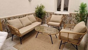 A cozy outdoor seating area with a sofa and two chairs, a small table, and a window with curtains.