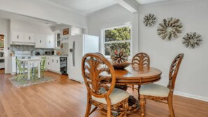 A modern kitchen with white cabinets, a dining table with chairs, and decorative wall art. - Seaside Serenity: 3BR/2BA Coastal Retreat
 (Tybee Island)