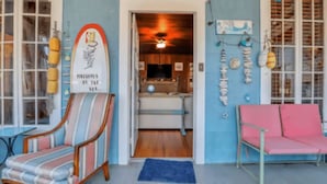 A room with a surfboard, a striped chair, and a pink sofa. - Seaside Serenity: 3BR/2BA Coastal Retreat
 (Tybee Island)