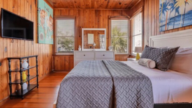 A wooden-paneled bedroom with a bed, dresser, and artwork. - Seaside Serenity: 3BR/2BA Coastal Retreat
 (Tybee Island)