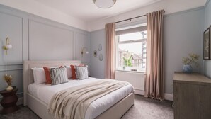 A bedroom with a large bed, a window with curtains, a bedside table, and a dresser. - Crescent Retreat- Windermere centre (Windermere)