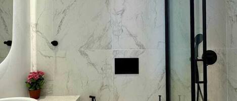 A modern bathroom with a marble wall, a glass shower enclosure, a white toilet, and a sink with a wooden shelf.