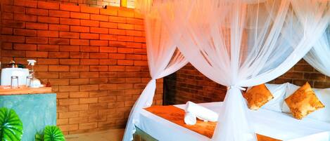 Una cama con dosel blanco, una pared de ladrillo y una mesita con artículos de aseo.