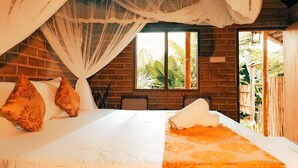 A bedroom with a large bed, a window with a view of greenery, and a brick wall. - LUNUVILA RESORT DICKWELLA (Dikwella)