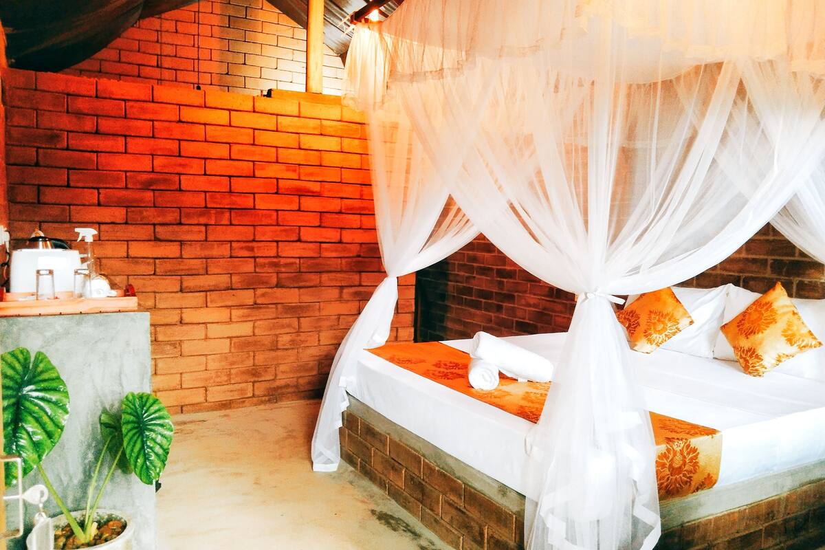 A room with a brick wall, a bed with a canopy, and a small table with toiletries.