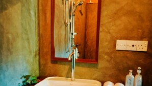 A bathroom with a white sink, a mirror, and a shower. There are toiletries on the counter. - LUNUVILA RESORT DICKWELLA (Dikwella)