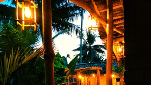 An outdoor dining area with wooden tables and chairs, surrounded by palm trees and a thatched-roof structure. - LUNUVILA RESORT DICKWELLA (Dikwella)