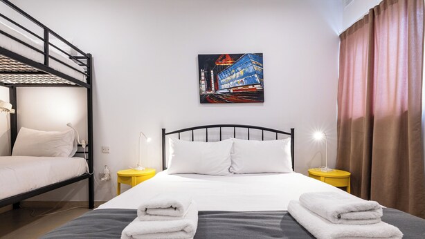 A hotel room with a bunk bed, a single bed, a painting on the wall, and a pair of towels on the bed. - Bright 2-bedroom Penthouse in Sliema, just steps from the promenade, Balluta beaches, cafés, and bus stops. Fully equipped with Wi-Fi, air conditioning, kitchen, and terrace — ideal for families or groups exploring Malta. (Tas-Sliema)