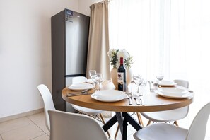 A dining area with a round table set for four, a refrigerator, and a vase with flowers. - Bright 2-bedroom Penthouse in Sliema, just steps from the promenade, Balluta beaches, cafés, and bus stops. Fully equipped with Wi-Fi, air conditioning, kitchen, and terrace — ideal for families or groups exploring Malta. (Tas-Sliema)