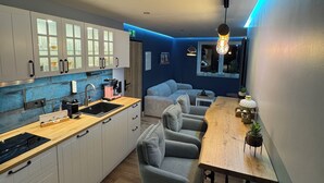 A modern kitchen with white cabinets, a wooden countertop, and a built-in oven. There is a dining area with a wooden table and grey chairs. - Boutique Apartments by Roy GmbH  (Oberhausen)
