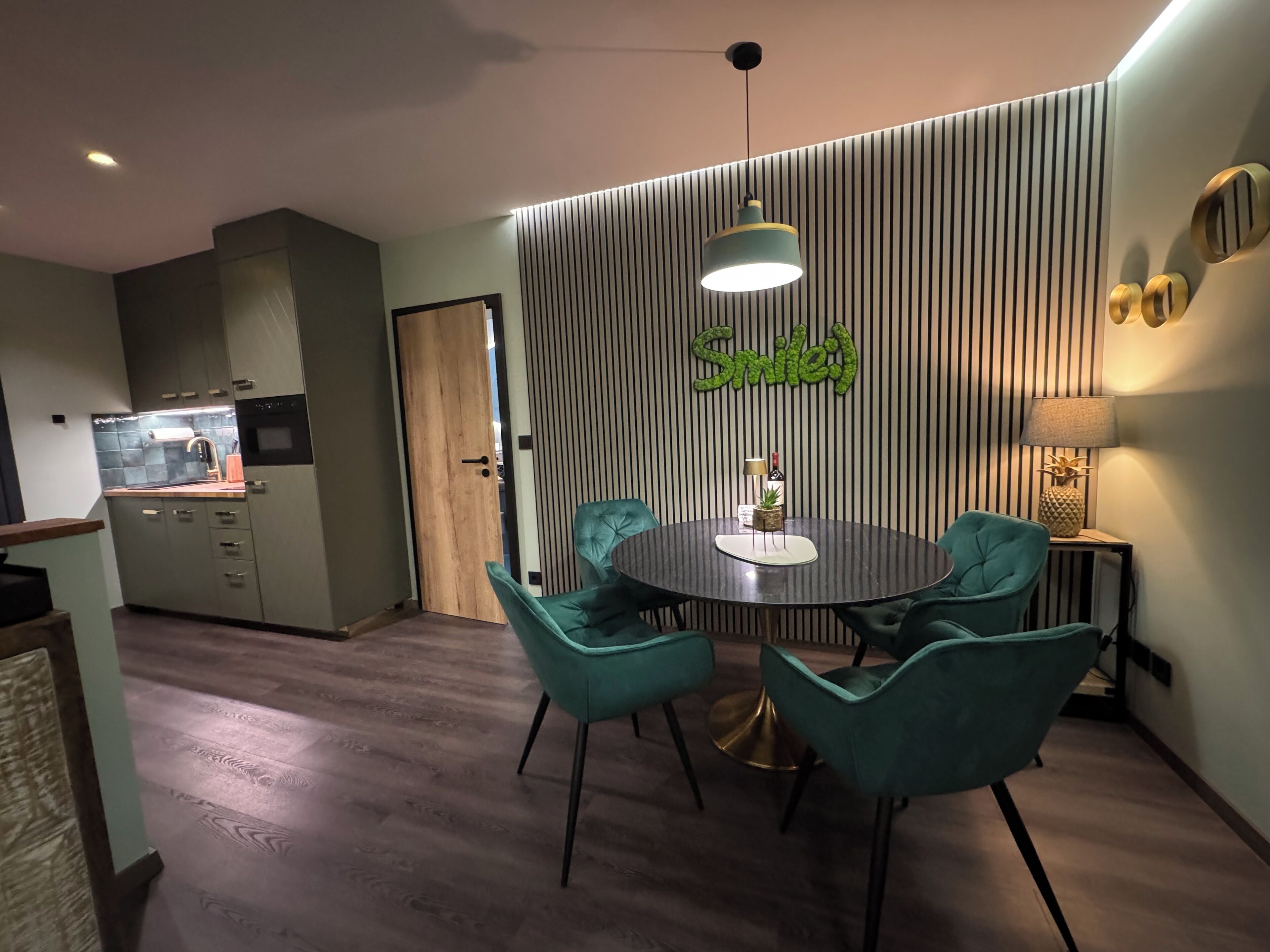 A modern kitchen with a dining area featuring teal chairs and a round table.