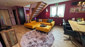Ein modernes Wohnzimmer mit einer Holztreppe, einem Ecksofa, einem runden Teppich und einem Essbereich mit Holztisch und Stühlen.