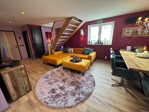 A modern living room with a wooden staircase, a sectional sofa, a round rug, and a dining area with a wooden table and chairs. - Boutique Apartments by Roy GmbH  (Oberhausen)