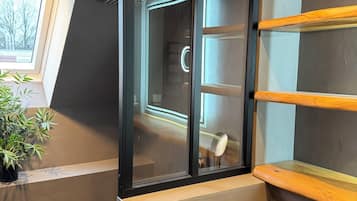 Un baño moderno con cabina de vidrio, estantes de madera y una planta en maceta.