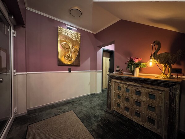 A hallway with a purple wall, a golden Buddha painting, a wooden cabinet with a glass door, and a decorative lamp. - Boutique Apartments by Roy GmbH  (Oberhausen)