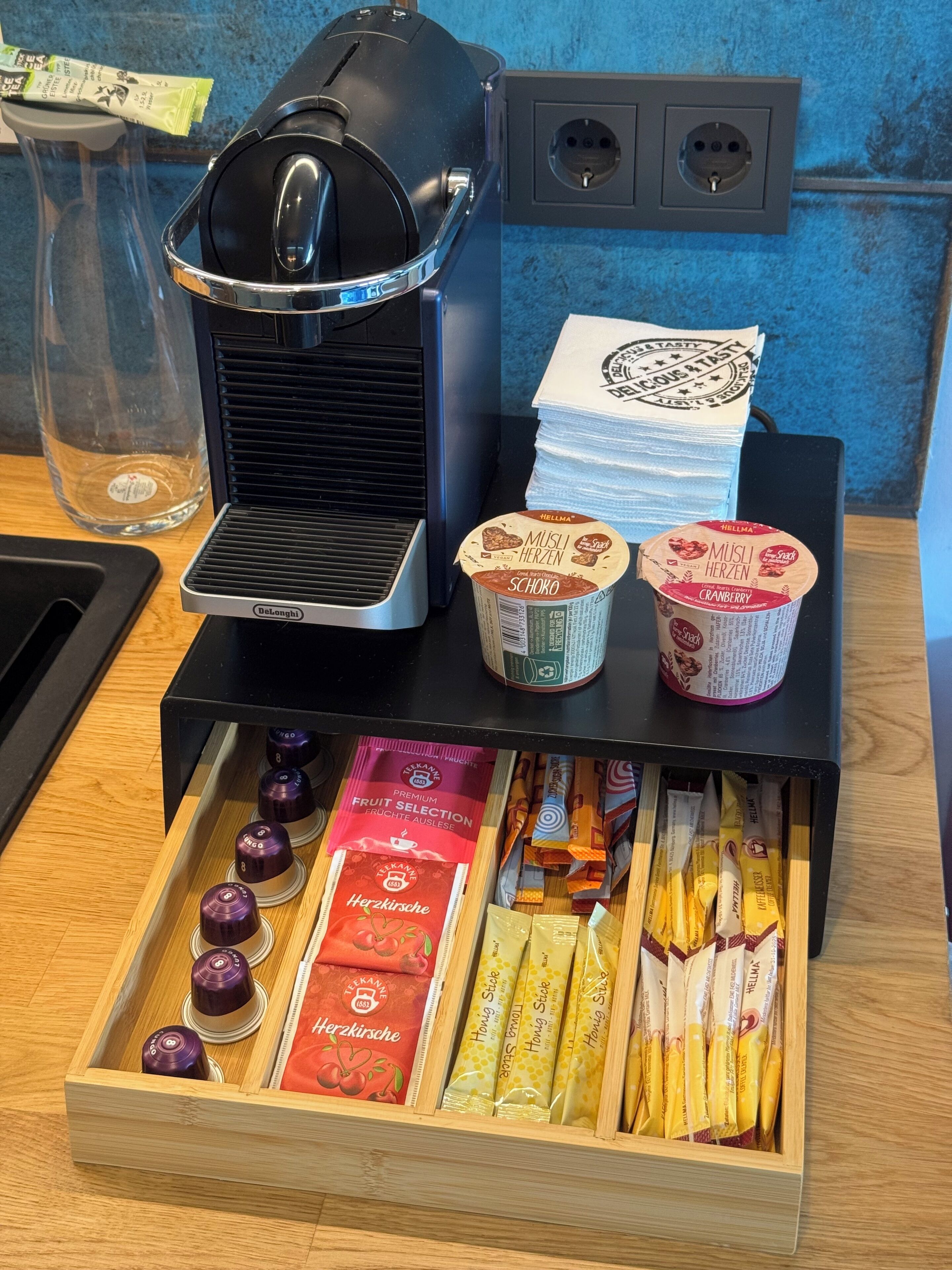 En kaffemaskine, to kopper kaffe og en skuffe med forskellige kaffekapsler.