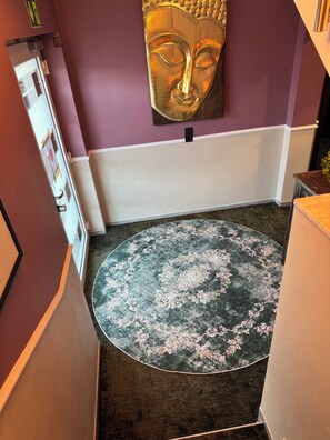 A room with a purple wall, a large Buddha statue, a round patterned rug, and a white baseboard. - Boutique Apartments by Roy GmbH  (Oberhausen)