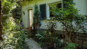 Una casa con un camino de piedra que lleva a la entrada, rodeada de exuberante follaje y plantas en macetas.