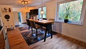 Una cocina moderna con comedor, piso de madera y ventanas amplias con vista a árboles.