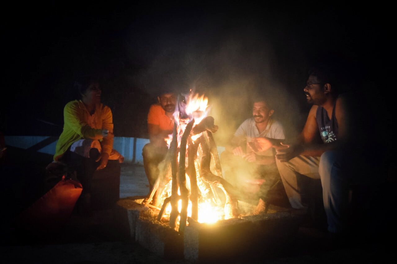 A group of people sitting around a campfire at night.