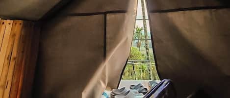 A tent with a bed, a window, and a view of greenery outside.
