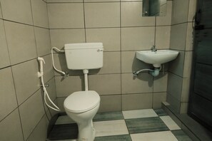Bathroom features a white toilet, sink, and mirror, set against a backdrop of large, square tiles and a checkered floor.