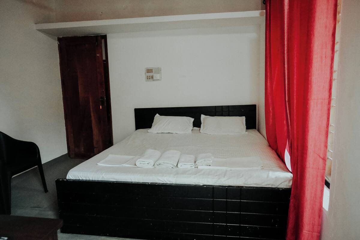 A neatly made bed with white linens and pillows, a wooden headboard, and a red curtain on the right.