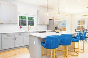 Una cocina moderna con gabinetes grises, una isla blanca y taburetes azules.