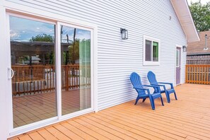 Una casa con terraza de madera, dos sillas Adirondack azules y un ventanal corredizo.