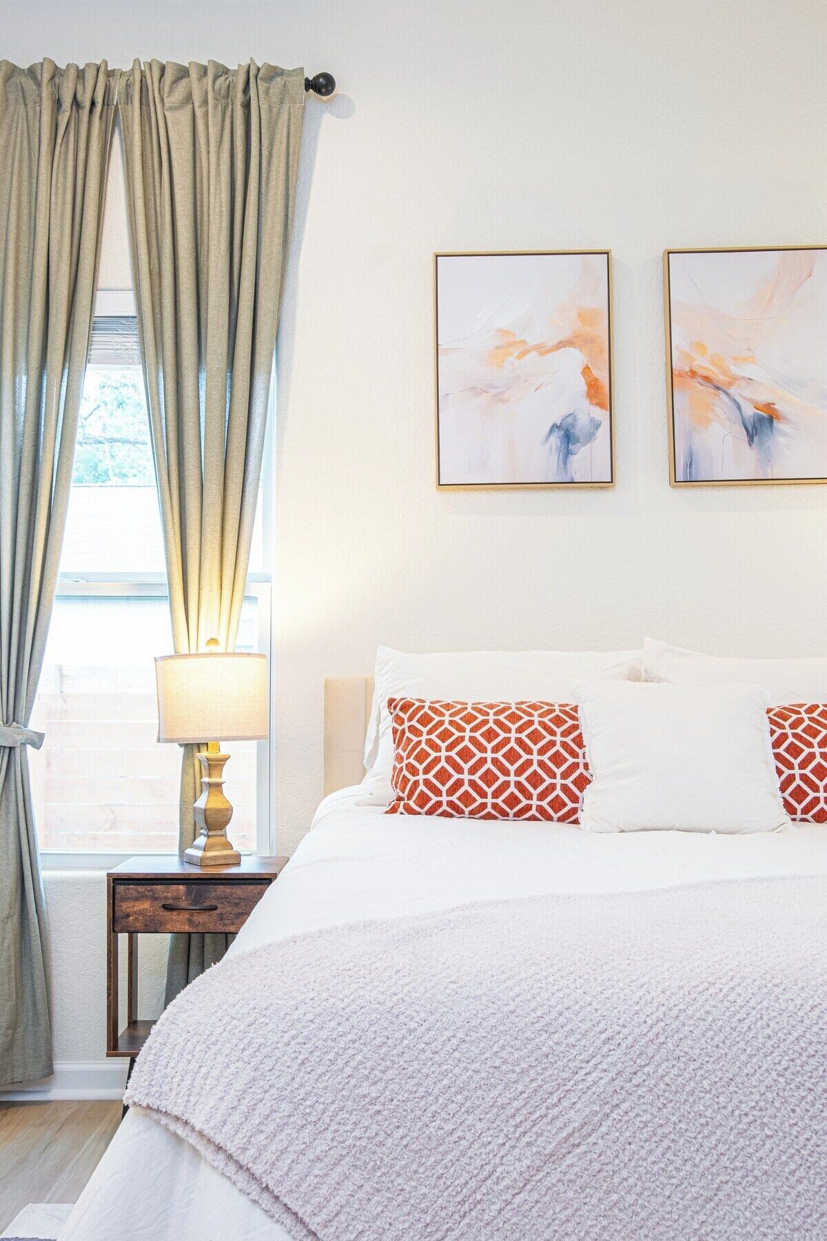A bedroom with a bed, a nightstand, a lamp, and two abstract paintings on the wall.