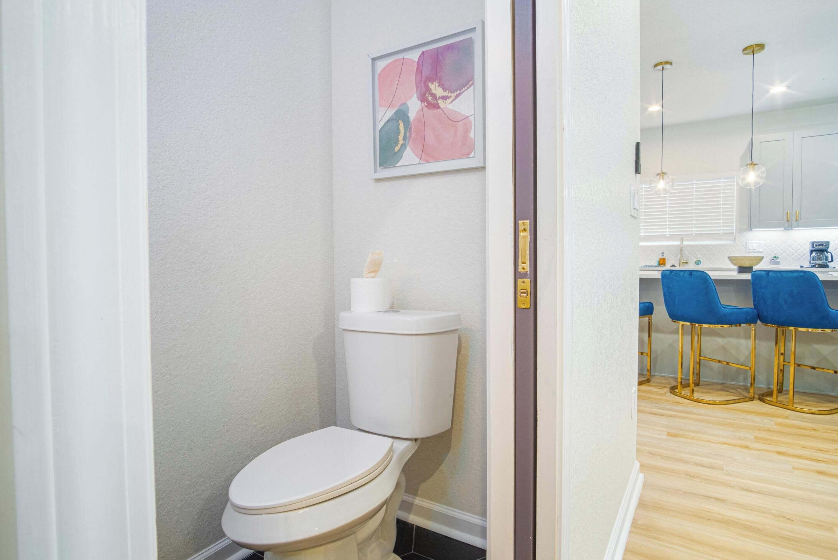 A modern bathroom with a toilet, a sink, and a blue bar stool.