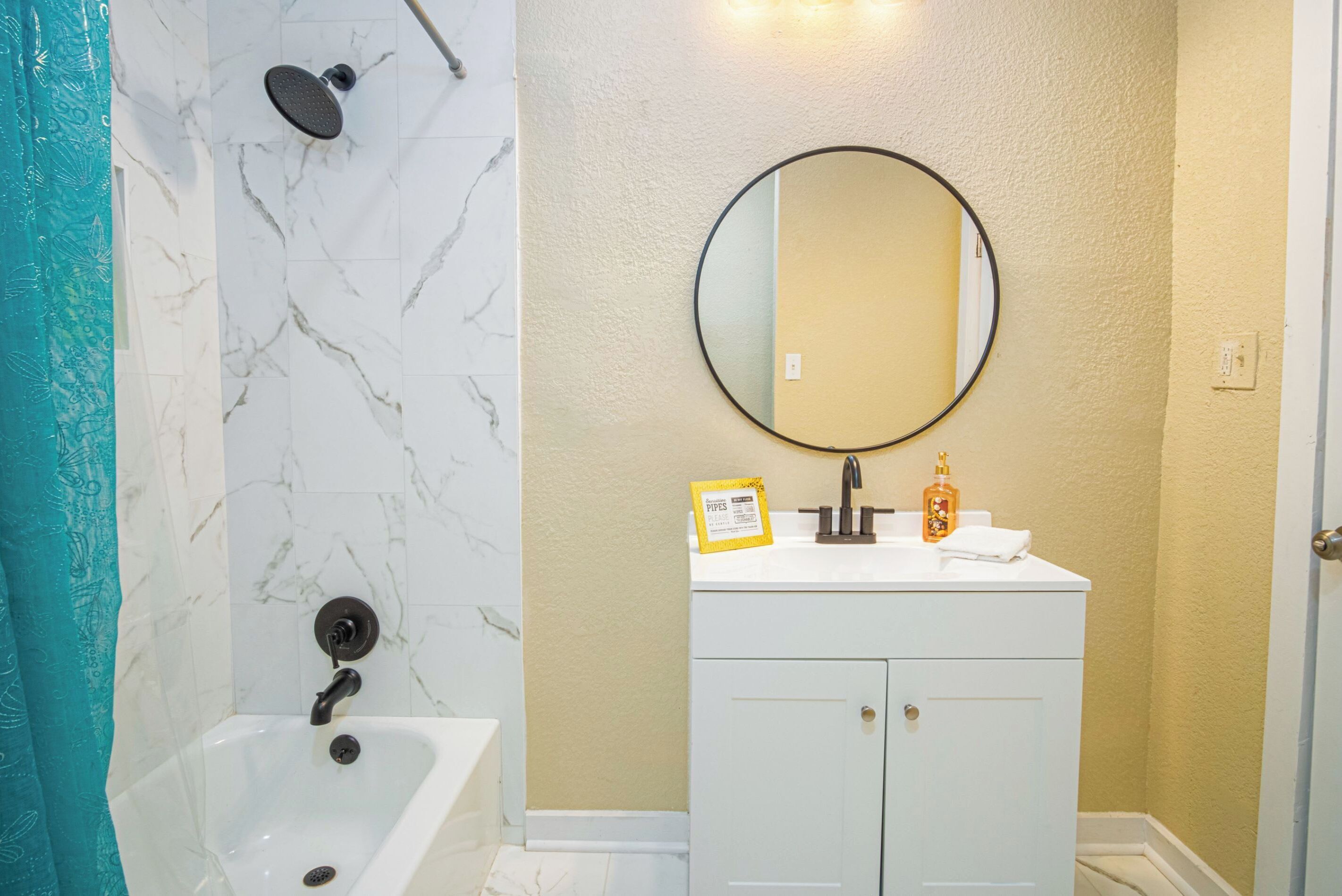 Une salle de bain avec un lavabo en marbre blanc, un miroir rond et une douche dotée d’un robinet noir.