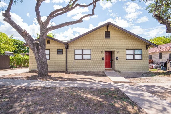 A two-story building with a red door and windows, surrounded by trees and a clear sky. - Modern Living 3br/2ba Close to Amazing Downtown (San Antonio)