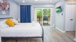 Un dormitorio con cama, ventilador de techo, televisión y vista al exterior.