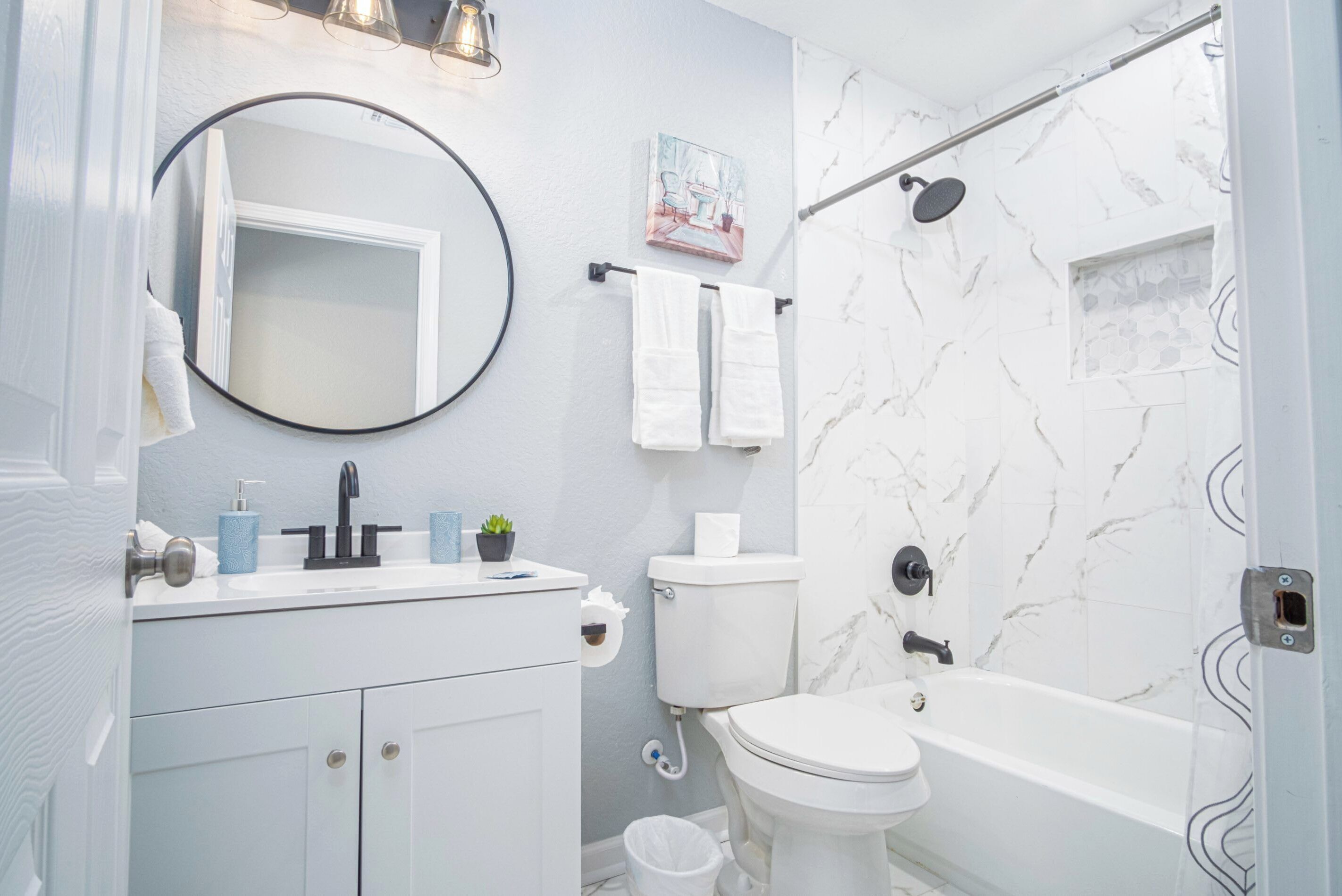 A modern bathroom with a white vanity, a round mirror, a toilet, a bathtub, and a shower.