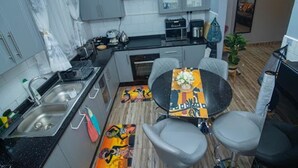 A compact kitchen with a sink, stove, and dining area with chairs. - 2bed-4guests-garden-nearcentre&attractions (Harare)