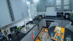 A compact kitchen with grey cabinets, a coffee machine, and a dining area with a table and chairs. - 2bed-4guests-garden-nearcentre&attractions (Harare)