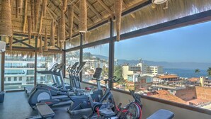 Une salle de sport équipée de matériel d’exercice et offrant une vue sur la ville et l’océan.