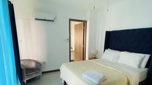 A hotel room with a bed, a chair, a nightstand, an air conditioning unit, and a door leading to another room. - Island vibes Oasis with a beautiful Pool (Kingston)