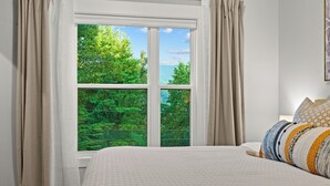 A bedroom with a large window, a bed with a quilt, and a nightstand.