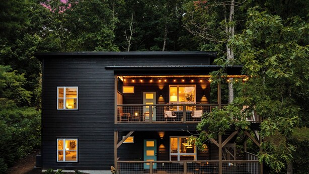 A two-story house with a balcony, surrounded by trees.