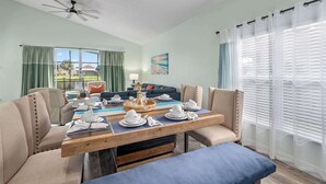 Ein Essbereich mit Holztisch, gedecktem Tisch für eine Mahlzeit, Deckenventilator und Blick ins Freie durch große Fenster.
