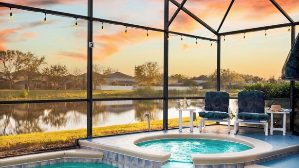 Poolbereich mit Whirlpool, Liegestühlen und Blick auf einen See im Sonnenuntergang.