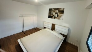 Une chambre à coucher avec un grand lit, une tête de lit, une œuvre d’art accrochée au mur et un luminaire au plafond.