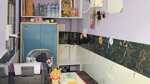 Ein Zimmer mit Schreibtisch, Deckenventilator, einem Regal mit diversen Gegenständen, einem gerahmten Bild und einer an der Wand montierten Steckdose.