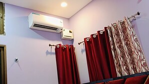 Ein Schlafzimmer mit Bett, roten Vorhängen, einem gemusterten Kopfstück und einer Klimaanlage an der Wand.