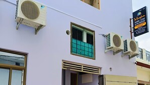 Ein zweistöckiges Gebäude mit Klimaanlagen, einem Fenster mit Gittermuster, einer Tür und einer kleinen Stufe zum Eingang.