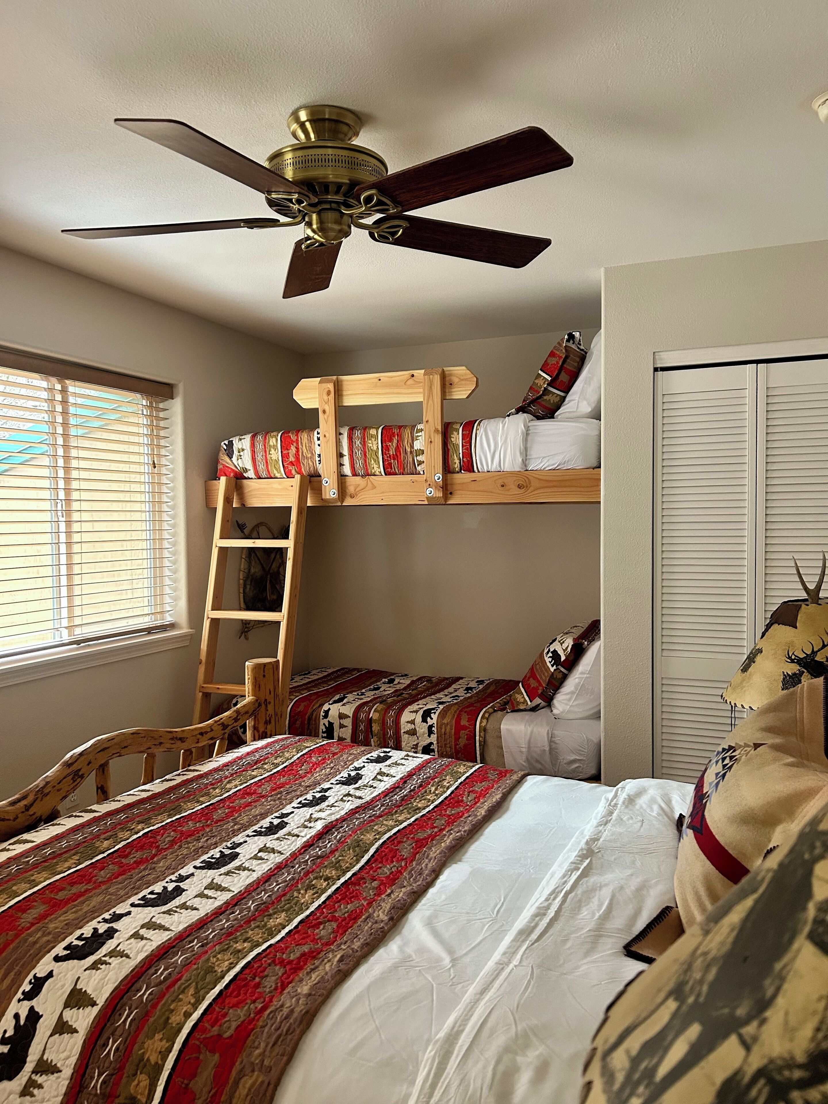 A bedroom with a bunk bed, a ceiling fan, a window with blinds, and a wardrobe.