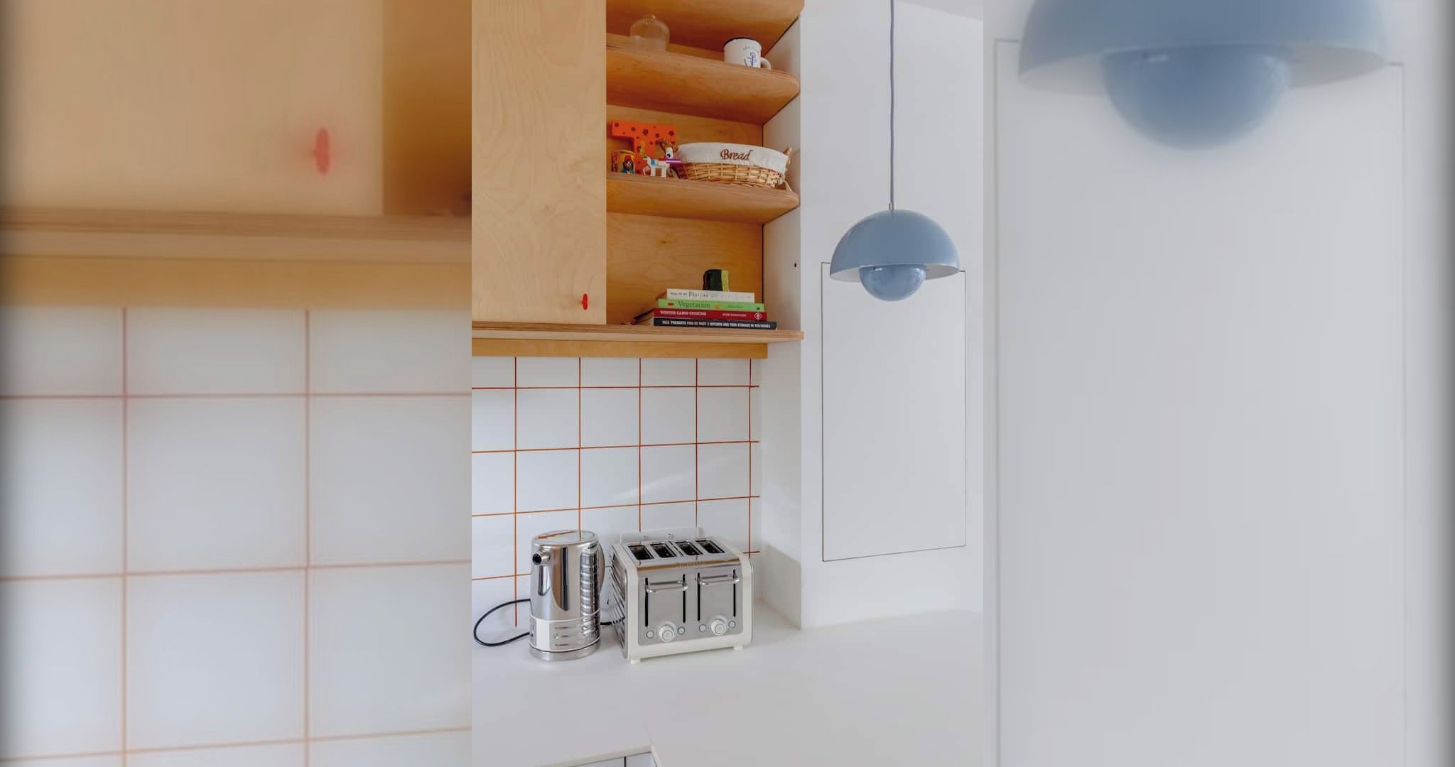 Una cocina con un revoque blanco en la pared, un estante de madera con una cesta que dice 'Pan' y una lámpara colgante azul.